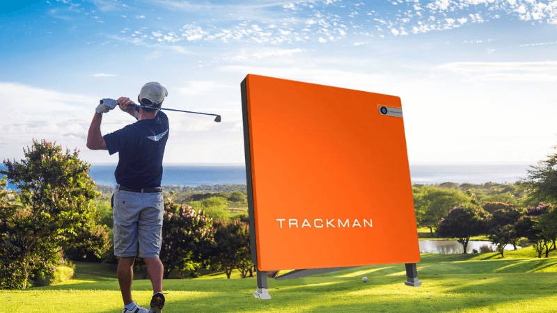 Golfeur réalisant un swing sur le parcours avec un radar TrackMan pour analyser ses performances.
